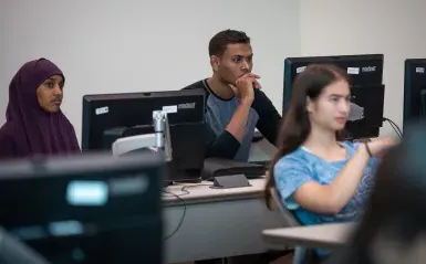 three students at computers in a classroom 